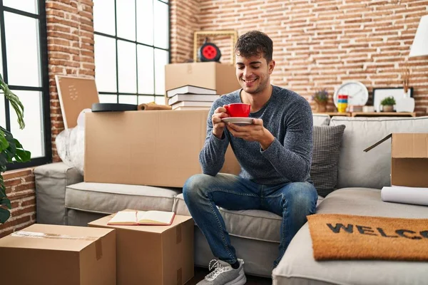 Genç İspanyol adam yeni evindeki kanepede kahve içiyor.