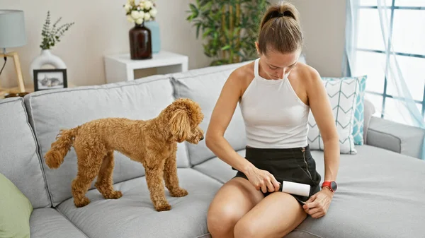 Young caucasian woman with dog using stick roll to clean pet hair at home