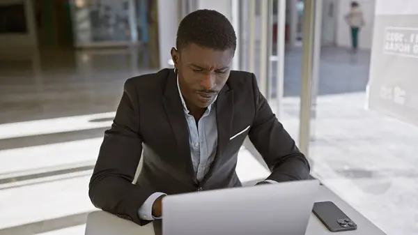 一位穿着西服的专注的非洲裔美国人在现代办公环境中的笔记本电脑上工作 传达着专业精神和奉献精神 — 图库照片