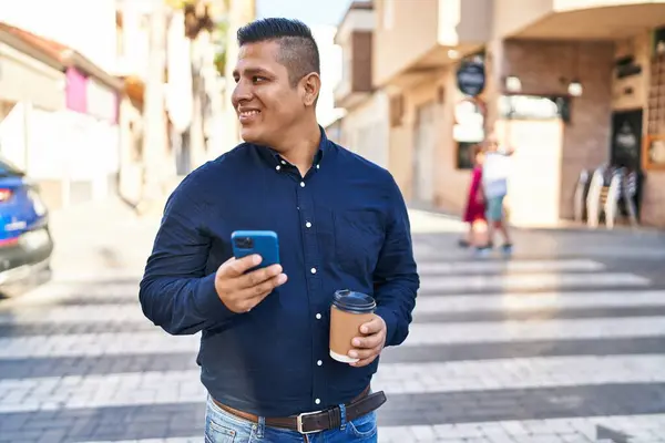 Young latin man using smartphone drinking coffee at street