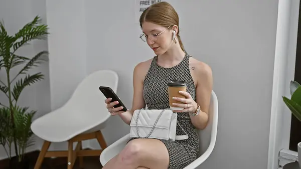 Young blonde woman sitting on chair using smartphone and earphones drinking coffee at waiting room