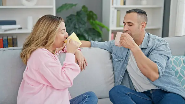 Man and woman couple drinking coffee sitting on sofa at home