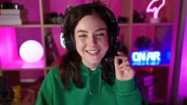 Smiling woman with headphones in a gaming room with neon lights at night.
