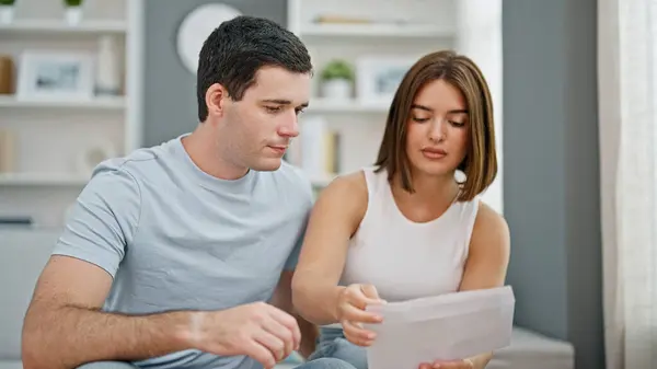 Beautiful couple reading document sitting on sofa looking upset at home