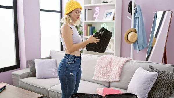 Young blonde woman making suitcase for holidays smiling at home