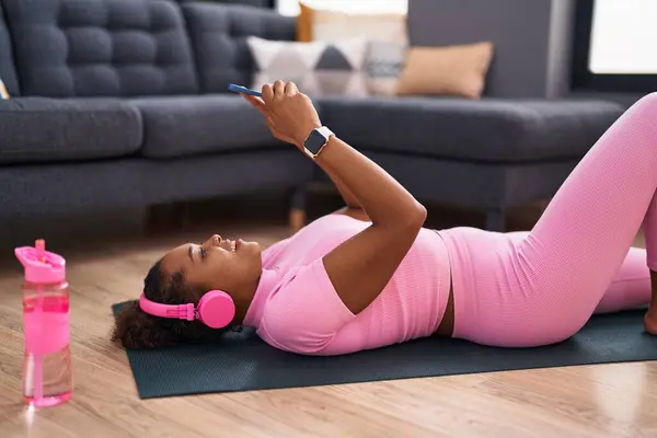 African american woman listening to music lying on yoga mat at home