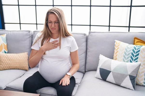 Young pregnant woman sitting on sofa suffering anxiety attack at home