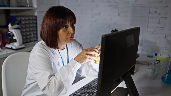 Mature hispanic woman scientist analyzing data on computer in lab.
