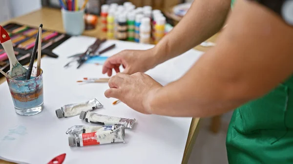 若いラテン芸術家男性は 活気に満ちた芸術のために設定されたスタジオテーブルにカラーペイントチューブを創造的に配置します — ストック写真