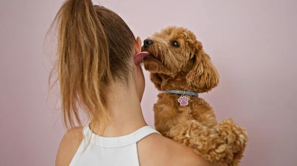 Young caucasian woman with dog kissing ear over isolated pink background