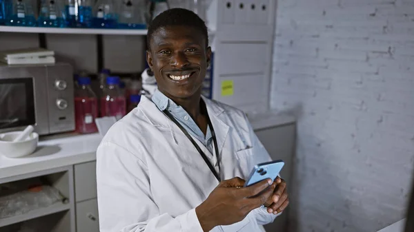 Homem Africano Sorridente Jaleco Usando Smartphone Ambiente Laboratório Transmitindo Moderno — Fotografia de Stock