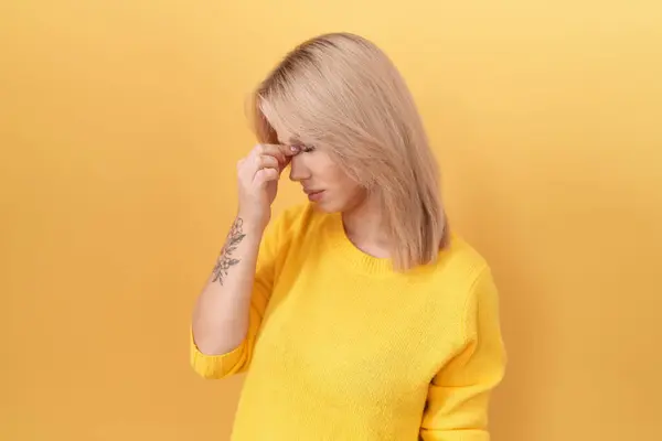 Young caucasian woman wearing yellow sweater tired rubbing nose and eyes feeling fatigue and headache. stress and frustration concept.