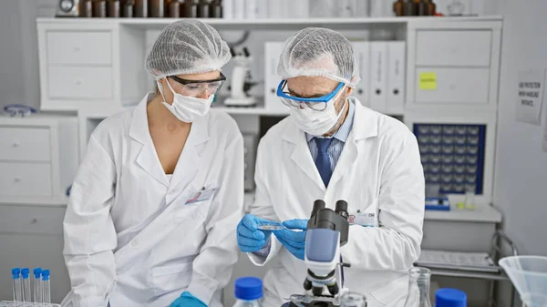 In the heart of science, two committed scientists, a man and a woman, masked and gloved, steadfastly holding a critical medical sample in their lab, defiant against covid19.