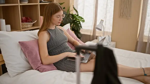 Young blonde woman business worker using laptop sitting on bed at hotel room