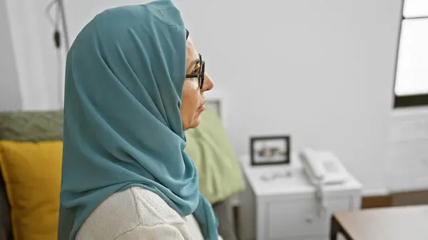 一个成熟的穆斯林女人 戴着眼镜 头戴头巾 在舒适的客厅里看起来很沉思 — 图库照片