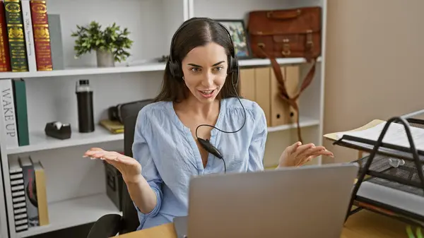 Glowing young hispanic woman is the picture of success in business - effortlessly juggles work, smiling during a video call at her office
