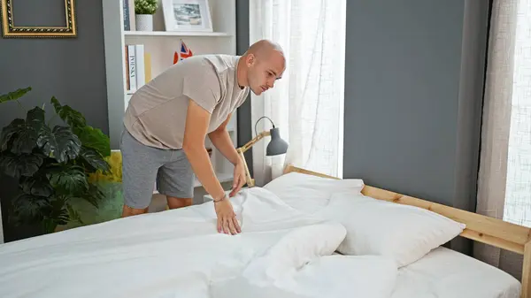 Young hispanic man make bed at bedroom