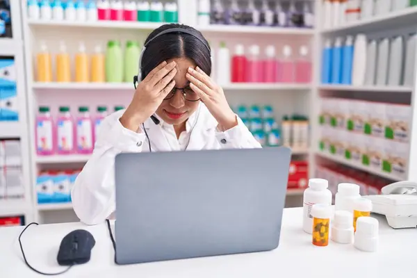Young arab woman working at pharmacy drugstore using laptop with sad expression covering face with hands while crying. depression concept.