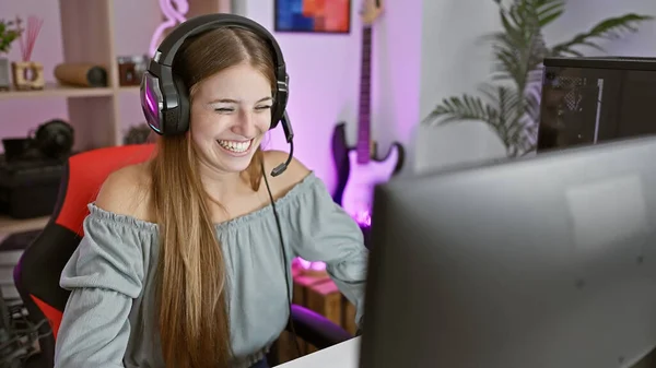 A cheerful young woman with headphones gaming in a vibrant indoor room at night.
