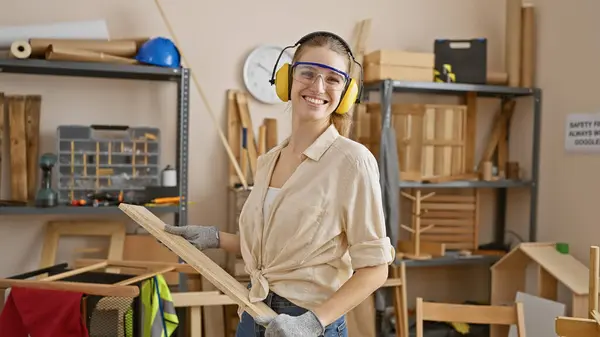 在木工车间里拿着木料 拿着安全装置微笑的女人 — 图库照片