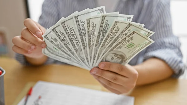 A man in a striped shirt displays american dollars in a well-lit office setting, suggesting themes of finance and business.