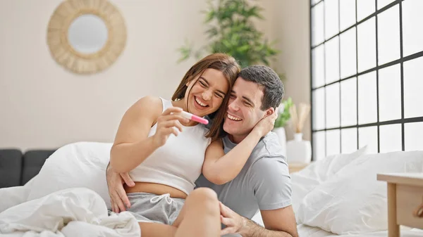Beautiful couple holding pregnancy test hugging each other smiling at bedroom
