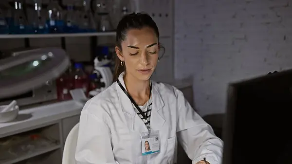 In the heart of science at night, a young, beautiful hispanic woman scientist sits seriously focused, working on her computer in the lab, immersed in groundbreaking medical research.