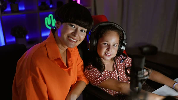 Unstoppable mother-daughter streamer duo, all smiles and immersed in the gaming bliss, rocking their headphones in gaming room.