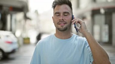 Şehir caddesinde cep telefonuyla konuşurken gülümseyen sakallı İspanyol bir adam..