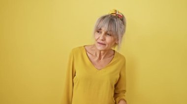 Gri at kuyruklu meraklı orta yaşlı kadın, parlak dedikodulardan hoşlanıyor, kulaklarını kapatıyor, sarı izole edilmiş arka planda sağırlık endişesini dile getiriyor..