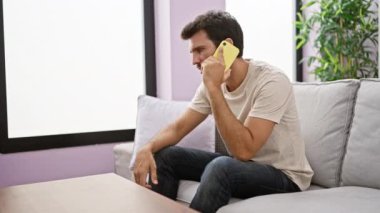 Sakallı genç bir adam modern dairesinde akıllı telefonunu incelerken hayal kırıklığına uğramış görünüyor..