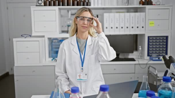 一位快乐的金发女科学家 戴着眼镜 身穿实验室外套 站在现代实验室里 佩戴着她的徽章 — 图库视频影像
