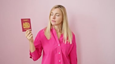Kendine güvenen sarışın kadın parmağını sana ve Kuzey İrlanda pasaportuna doğrultarak izole edilmiş pembe arka plandaki kameraya ciddi bir şekilde bakıyor.