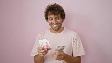 Pembe arka planda İzlanda kronu banknotları tutan mutlu genç adam, neşe ve finansal rahatlık hissi yayıyor..