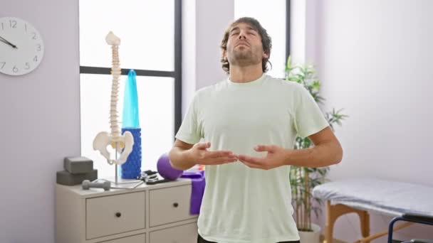 ひげを被った若者は 理学療法クリニックで瞑想し 目を閉じて天井に向かって手を開きます — ストック動画