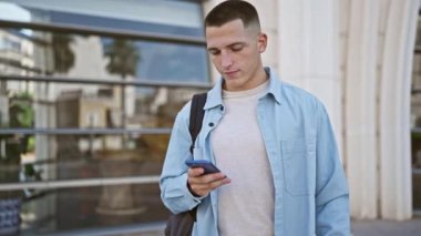 Gündelik giyinmiş genç bir adam şehir ortamında akıllı telefon tutarken başparmağını kaldırıyor..