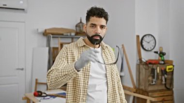 Güvenlik gözlüklü İspanyol genç adam iyi donanımlı bir marangozluk atölyesinde duruyor, profesyonel ve yetenekli bir zanaatkârı somutlaştırıyor..