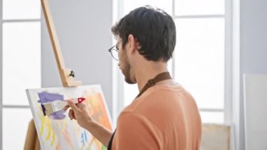 Parlak bir sanat stüdyosunda sakallı bir adam tuvale resim yapıyor..