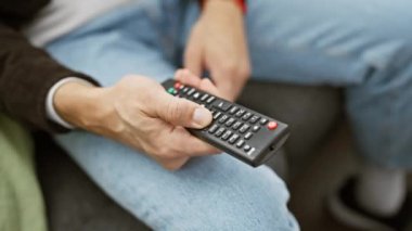 Ev ortamında bir kanepede rahatça oturup televizyon seyretmeye hazır bir adam..