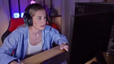 Kulaklıklı, karanlık bir oyun odasında bilgisayar kullanan odaklanmış genç bir kadın.