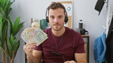 Kulaklık takmış genç adam gururla zaferle parıldayan Romanya lei banknotlarını ofiste yükseltiyor!