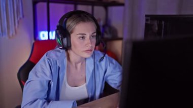 Ev ofisinde geceleri kulaklık takan odaklanmış genç bir kadın oyun oynarken duygularını sergiliyor..