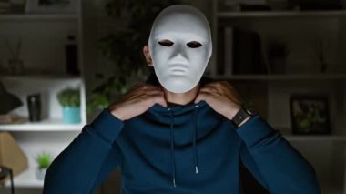 Beyaz maskeli ve mavi kapüşonlu bir adam ofiste duruyor ve gizemli bir atmosfer yaratıyor..