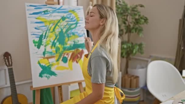 Una Mujer Rubia Confiada Artista Estudio Con Una Pintura Abstracta — Vídeo de stock