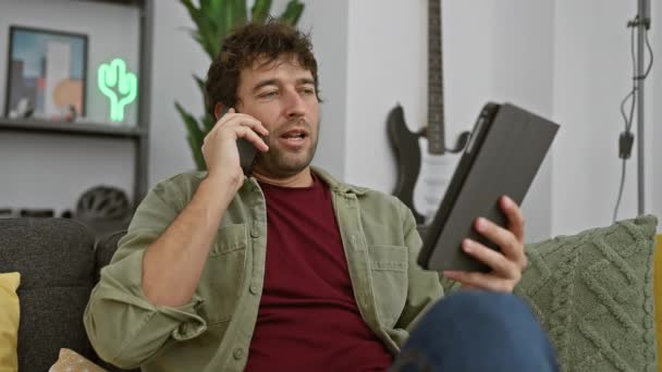 Hombre Hispano Habla Por Teléfono Mientras Sostiene Tableta Sala Estar — Vídeos de Stock