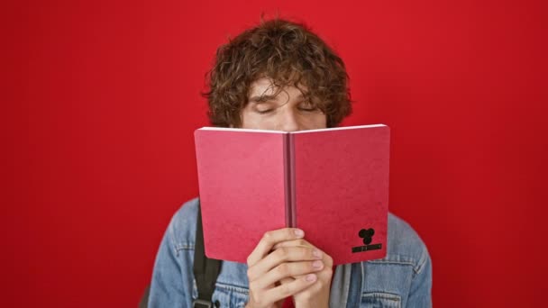 Pria Berambut Keriting Bersembunyi Balik Notebook Merah Terhadap Latar Belakang — Stok Video
