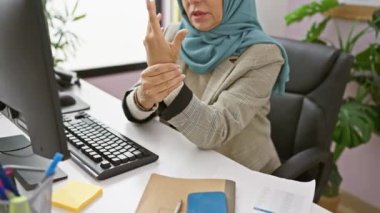 İş yerinde bilgisayar ve bitki ile bilek ağrısı çeken tesettürlü olgun Müslüman bir kadın..