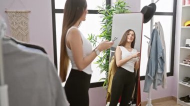 Gülümseyen bir kadın, parlak bir elbise odasında ayna ve askılı giysilerle telefon kullanıyor..