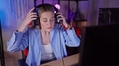 Kulaklık takan odaklanmış bir kadın geceleri neon ışıklı oyun odasında bilgisayar kullanıyor..