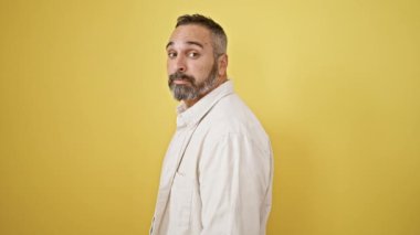 Gri sakallı, olgun, yakışıklı bir adam sarı izole edilmiş arka plana şaşırdığını ifade ediyor.